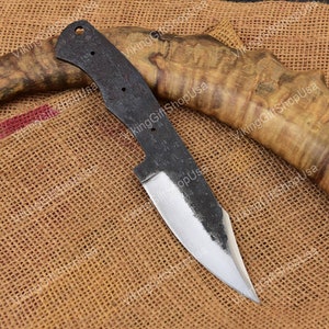 May include: A forged steel knife blade with a partially sharpened edge. The blade has a dark, textured finish and a pointed tip. The handle area has three holes and a hole for a lanyard. The knife is displayed on a burlap surface.