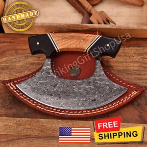 May include: A handmade, Damascus steel cleaver with a wooden handle and a leather sheath. The cleaver has a unique, swirling pattern on the blade. The image also includes the text "100% Handmade 100%".