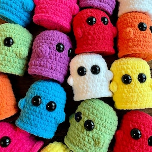 May include: A collection of colorful, crocheted ghost-like figures. The figures are in various bright colors, including pink, purple, green, blue, orange, white, red, and yellow. Each has large, black button eyes.
