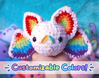 Puede incluir: Un murciélago de peluche hecho a mano con alas y detalles de colores del arcoíris. El murciélago es blanco con motas coloridas y tiene ojos grandes y negros. Las alas presentan un degradado de colores del arcoíris. El texto "Customizable Colors!" está en la parte inferior.