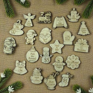 May include: A collection of laser-cut wooden Christmas ornaments with various shapes and text, including a snowman, angel, and Santa. The ornaments feature phrases like "Hot Cocoa" and "Movie Night."