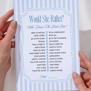 May include: A light blue and white striped game card titled "Would She Rather?" with a decorative border. The card lists various choices for a bridal shower game, such as "take a road trip" and "fly to a destination".