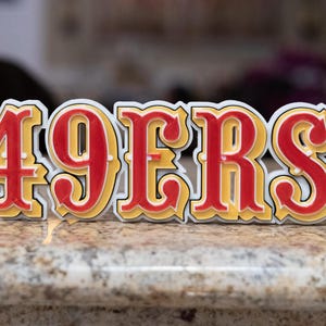 May include: A white, red and yellow 3D sign that reads "49ERS".