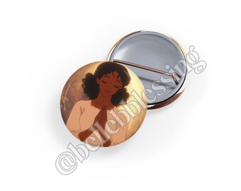 Pode incluir: Um botão redondo com uma imagem de uma jovem com pele morena e cabelo castanho longo. Ela está vestindo um vestido branco e tem as mãos juntas em oração. O fundo é amarelo e laranja suave.