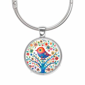 May include: A silver key ring with a round charm featuring a colorful bird perched on a tree branch surrounded by flowers.