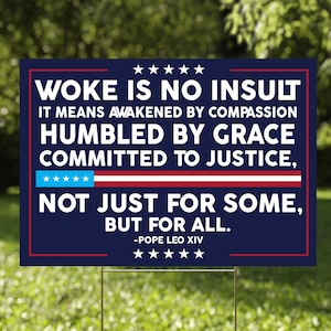 May include: A rectangular sign with the text "WOKE IS NO INSULT" in white letters on a navy blue background. The sign also includes the text "IT MEANS AWAKENED BY COMPASSION, HUMBLED BY GRACE, COMMITTED TO JUSTICE, NOT JUST FOR SOME, BUT FOR ALL."