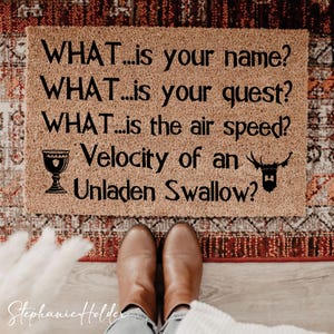 Puede incluir: Felpudo rectangular de fibra natural con el texto "WHAT...is your name? WHAT...is your quest? WHAT...is the air speed? Velocity of an Unladen Swallow?" en negro. Incluye un cáliz y un ciervo.