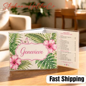 Pode incluir: Um porta-cartões Mah Jongg de plástico transparente com um design floral tropical. O suporte apresenta uma flor de hibisco rosa, folhas verdes e o nome "Genevieve" em uma moldura decorativa. O lado direito exibe um cartão de referência rápida.
