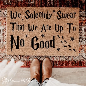 May include: A rectangular coir doormat with the phrase "We Solemnly Swear That We Are Up To No Good" in black lettering. The mat features star and footprint graphics. Brown boots are visible in the foreground.