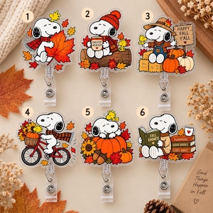 Könnte beinhalten: Sechs Acryl-Ausweishalter mit Snoopy in herbstlichen Szenen. Die Motive zeigen Snoopy mit Ahornblatt, einer Tasse mit der Aufschrift Sweater Weather, einem Schild mit Happy Fall Y'all, auf einem Fahrrad, auf einem Kürbis und lesend mit einem Buch namens Fall Kindness sowie einem Stapel Bücher mit der Aufschrift Pumpkins, Good Books, Cozy Days.