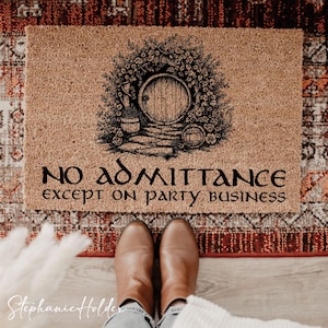 May include: A rectangular doormat with a Hobbit-themed design. The mat is tan with a black illustration of a round door surrounded by foliage. The text "NO ADMITTANCE except on party business" is printed below the illustration.