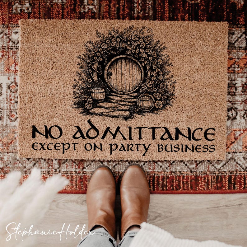 May include: A rectangular doormat with a Hobbit-themed design. The mat is tan with a black illustration of a round door surrounded by foliage. The text "NO ADMITTANCE except on party business" is printed below the illustration.