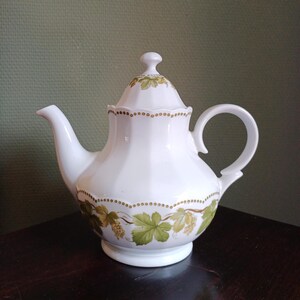 May include: White porcelain teapot with a lid and a handle. The teapot has a floral design with green leaves and yellow grapes.