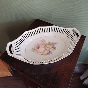 Könnte beinhalten: Weiße Porzellanservierschale mit einem zarten Blumendesign mit einer rosa und gelben Rose. Die Schale hat ein Gittermuster am Rand und zwei Griffe.