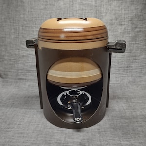 Könnte beinhalten: Ein brauner Keramik-Fonduetopf mit einem Metallständer und einem Brenner. Der Topf hat ein gestreiftes Design und einen Deckel.