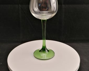 May include: A clear wine glass with a green stem and base. The glass has a rounded bowl and a long, slender stem. The base is circular. The glass is on a white surface against a black background.