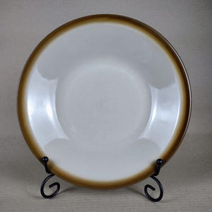 May include: A white ceramic bowl with a brown rim. The bowl is on a black metal stand.