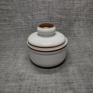 May include: White ceramic sugar bowl with a brown lid. The lid has a rounded top and a brown band around the edge.