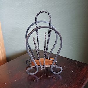 Op de afbeelding: Zwarte metalen servetthouder met een houten basis. De houder heeft een decoratief, gedraaid ontwerp.
