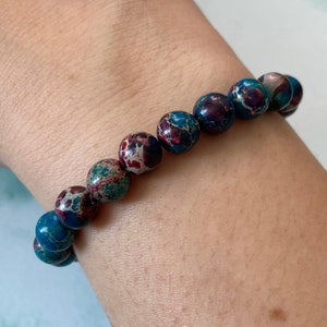May include: A bracelet made of blue, red and white jasper beads. The beads are round and have a speckled pattern.