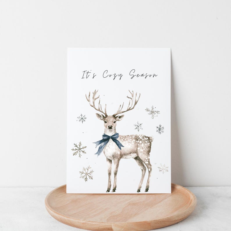 May include: A watercolor illustration of a deer with a blue bow tie, surrounded by snowflakes. The text "It's Cozy Season" is written at the top of the image.