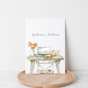 Pu&ograve; includere: Un'illustrazione ad acquerello di una scrivania con un laptop, una zucca e foglie autunnali in un vaso. Il testo "Welcome Autumn" &egrave; scritto sopra la scrivania.