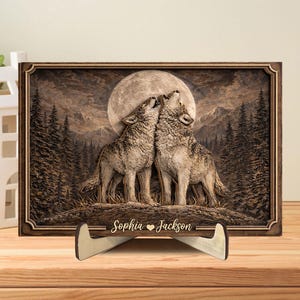 May include: A wooden framed artwork depicting two wolves howling at the moon in a forest setting. The artwork is displayed on a wooden stand. The names "Sophia Jackson" are engraved on the stand.