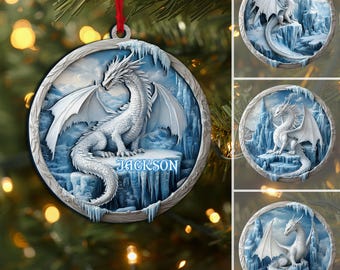 May include: A round Christmas ornament featuring a white dragon with outstretched wings, perched on a blue icy landscape. The ornament has a silver frame and a red ribbon for hanging. The name "JACKSON" is displayed on the icy platform.