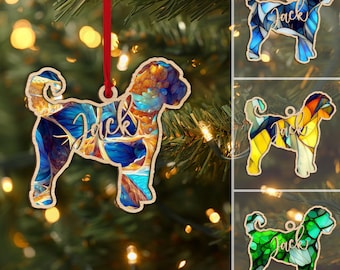 May include: Wooden dog-shaped Christmas ornament with a stained-glass effect. The ornament is in shades of blue, orange, and gold, with the name "Jack" in cursive. Additional ornaments in blue, yellow, and green are also shown.