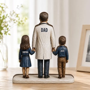 May include: A wooden figurine depicting a father figure holding the hands of a girl and a boy. The father wears a white coat with "DAD" on the back. The girl's jacket says "SOPHIA" and the boy's says "JACK". The base is a light brown color.