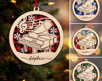 May include: Wooden Christmas ornament featuring a grand piano design with the year 2024. The ornament has a red and black plaid background and the name "Sophia" is written in cursive. Includes musical notes and snowflakes.