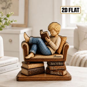 May include: A decorative figurine of a person with blonde hair reading a book while sitting on a small sofa. The sofa rests on a stack of books with the text "Just A Boy Who Loves Books" and "Brown" printed on the side. The base is wooden.