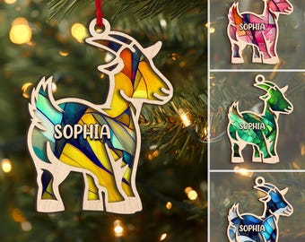 Könnte beinhalten: Holzziegenornament mit Buntglasdesign in Gelb, Blau und Grün. Der Name "SOPHIA" ist auf dem Körper der Ziege abgebildet. Der Schmuck hängt an einem roten Band, perfekt für die Weihnachtsdekoration.