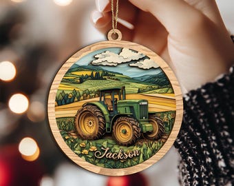Peut inclure: Ornement de Noël rond en bois représentant un tracteur vert dans un champ de tournesols, sous un ciel bleu nuageux. Le nom "Jackson" est inscrit en bas. L'ornement est suspendu par une ficelle dorée.