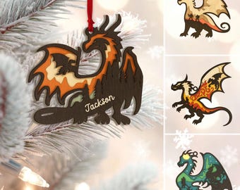May include: Wooden dragon Christmas ornament with a red ribbon. The dragon is brown, orange, and tan, with the name "Jackson" on the body. Additional dragon ornaments in different colors are also shown.