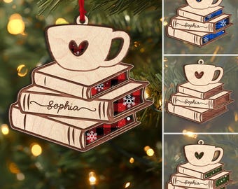May include: Wooden Christmas ornament featuring a coffee cup with a heart cutout, resting on a stack of books. The books have plaid and snowflake details, with the name "Sophia" scripted on them. The ornament hangs from a red ribbon.