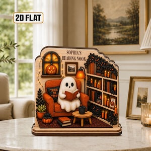 May include: A flat wooden decorative display featuring a ghost sitting in an orange armchair reading a book. The scene includes a bookshelf with candles, a pumpkin in a window, and the text "SOPHIA'S READING NOOK" printed at the top.