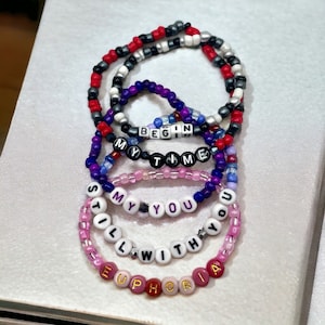 May include: Five colorful beaded bracelets with the words "BEGIN MY TIME", "STILL MY YOU", and "EUPHORIA" spelled out in white letters.
