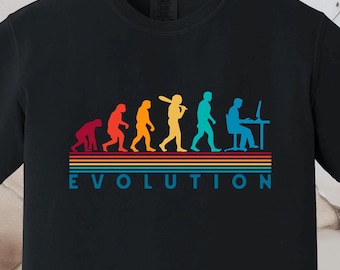 May include: Black t-shirt featuring a colorful graphic of the evolution of man, from ape to computer user. The word "EVOLUTION" is printed in blue, green, yellow, orange, and red on the shirt.