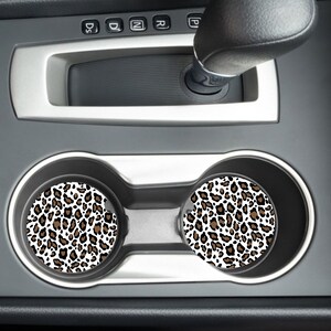 May include: Two brown and white leopard print car coasters in a car cup holder.