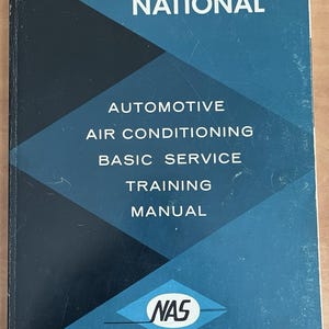 May include: A rectangular training manual with a dark blue and black geometric cover. The white text reads NATIONAL AUTOMOTIVE AIR CONDITIONING BASIC SERVICE TRAINING MANUAL. A white diamond logo with the letters NAS is at the bottom center.