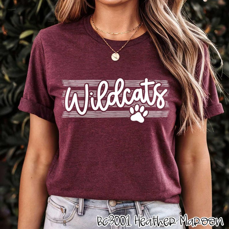 Op de afbeelding: Een maron heather t-shirt met de tekst "Wildcats" in wit met een witte pootprint eronder. Het shirt heeft een ronde hals en korte mouwen.
