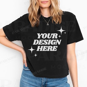 May include: A black cropped t-shirt with the text "YOUR DESIGN HERE" in white lettering and a few white stars. The shirt is being worn by a person with long blonde hair and blue jeans.