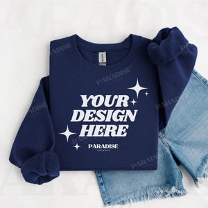 May include: A navy blue crew neck sweatshirt with the text "YOUR DESIGN HERE" in white, and star graphics. The sweatshirt is displayed with denim shorts. The mock-up is on a white background.