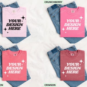 May include: Four t-shirts in shades of pink and red, each with the text "YOUR DESIGN HERE". The shirts are folded on top of blue denim jeans. The colors are: light pink, bright pink, coral, and maroon.