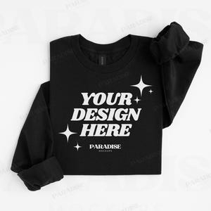 May include: Black long-sleeve shirt with the text "YOUR DESIGN HERE" in white, along with star graphics. The shirt is from Paradise Mockups.