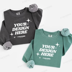 Puede incluir: Dos sudaderas de manga larga, una gris carbón y otra verde azulado, con el texto "YOUR DESIGN HERE" en blanco. Las sudaderas tienen puños enrollados y la palabra "PARADISE" está impresa debajo.