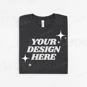 Könnte beinhalten: Ein dunkelgraues T-Shirt mit dem Text "YOUR DESIGN HERE" in Weiß. Das Shirt hat einen Used-Look und kleine weiße Sterne.