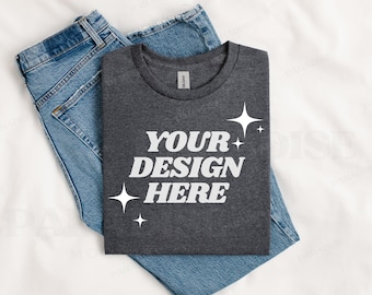 May include: A dark gray t-shirt with the text "YOUR DESIGN HERE" in white lettering and small white stars. The t-shirt is folded and placed on top of a pair of blue jeans.