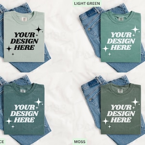 May include: Four t-shirts in various shades: bay, light green, blue spruce, and moss. Each shirt displays the text "YOUR DESIGN HERE" in white. The shirts are placed on blue denim jeans.